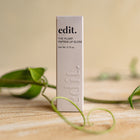 Lip gloss container labeled 'edit.' on a wooden surface with green leaves.