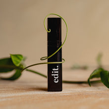 Black cylindrical product with 'edit.' branding on a wooden surface with green leaves.