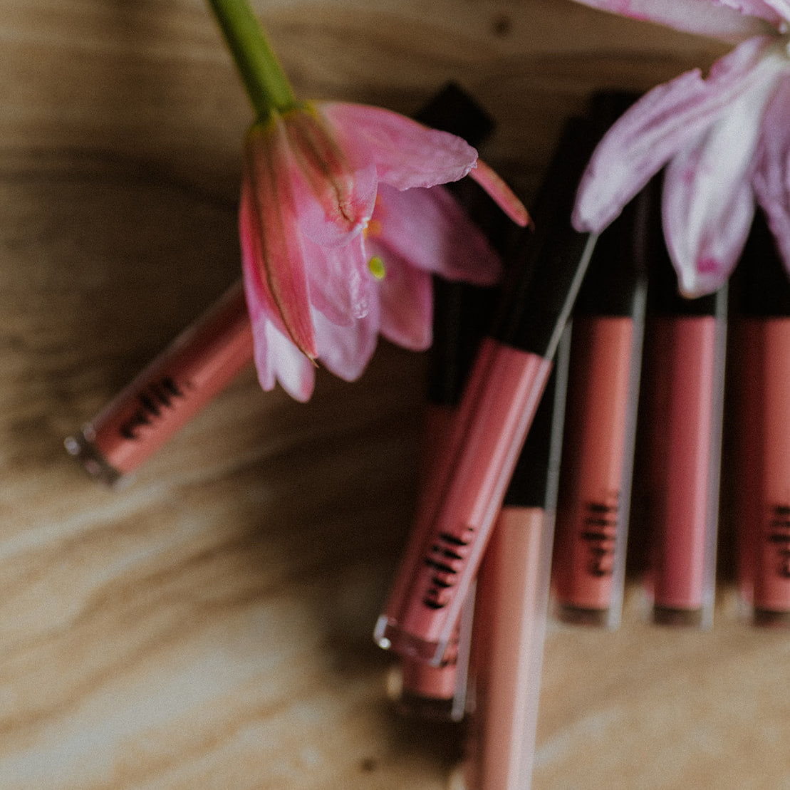 Lip glosses with pink flowers on a wooden surface
