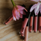Lip glosses with pink flowers on a wooden surface